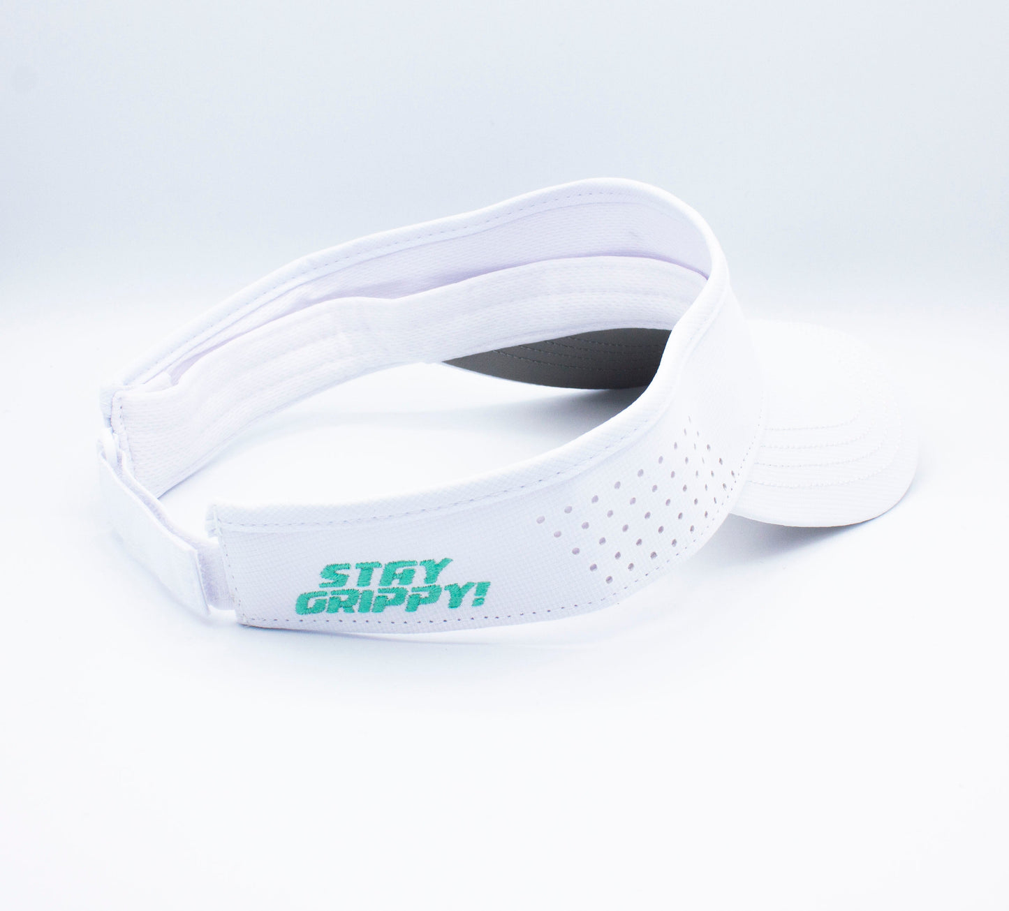The Bodhi Performance ICON Visor is a white sports visor with perforated holes along the band and “STAY GRIPPY!” printed in green on the side, shown slightly open to display its interior and adjustable strap.