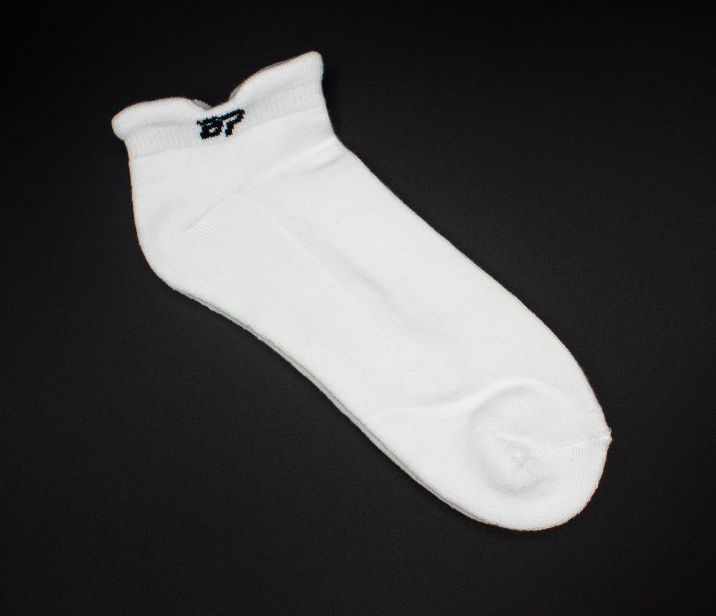 The Bodhi Performance Performance Sock in white features a small black 97 on the cuff, breathable support, a slightly ribbed top, and reinforced toe and heel areas for comfort. Displayed against a solid black background.