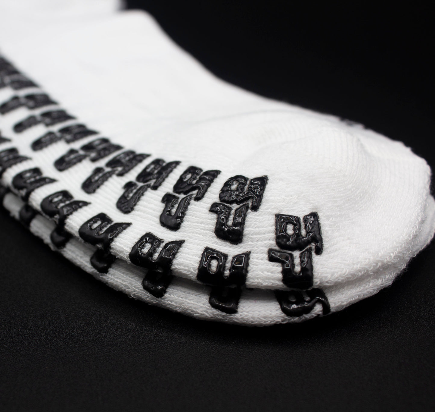 A close-up of Bodhi Performance's Performance Socks - GRIPtech™, featuring black silicone anti-slip pads in stylized patterns on the white sole, displayed against a black background.