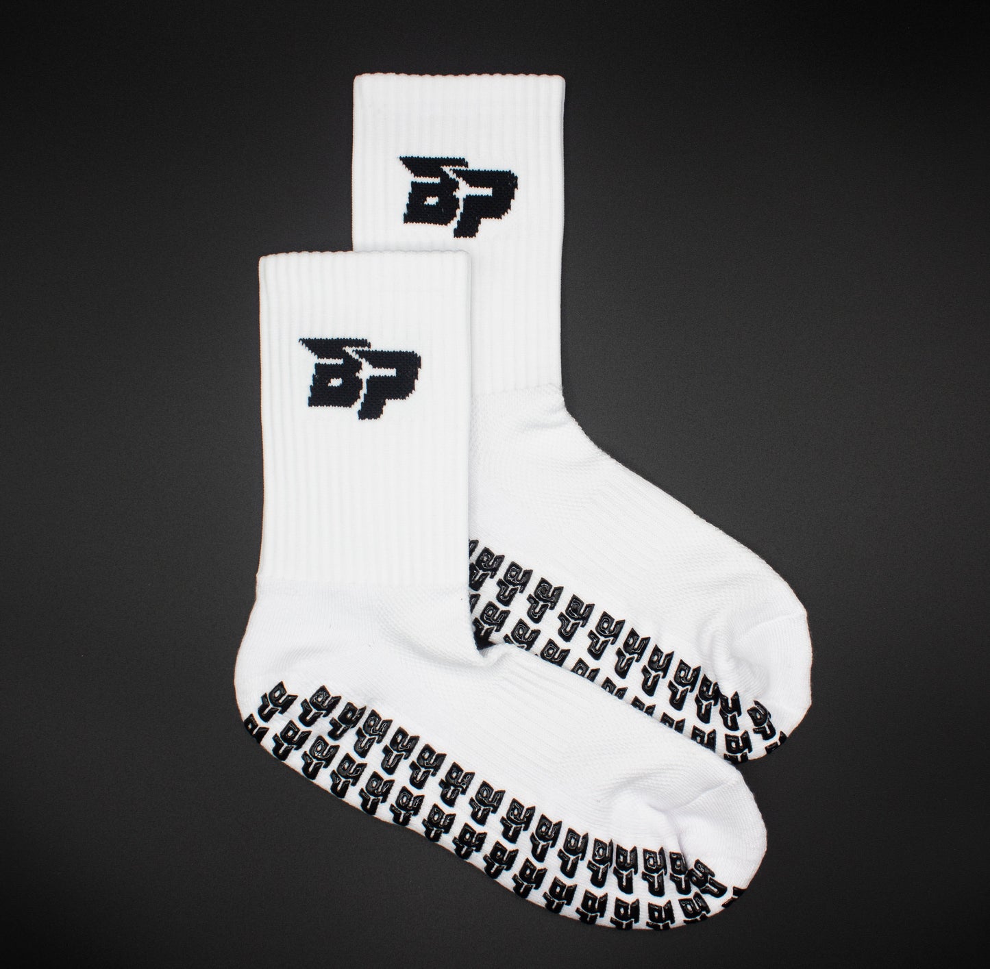 Performance Socks - GRIPtech™ by Bodhi Performance: white crew socks with black BP logo on the cuffs and repeated BP text in black silicone grip on the soles for traction. Displayed flat on a solid black background.