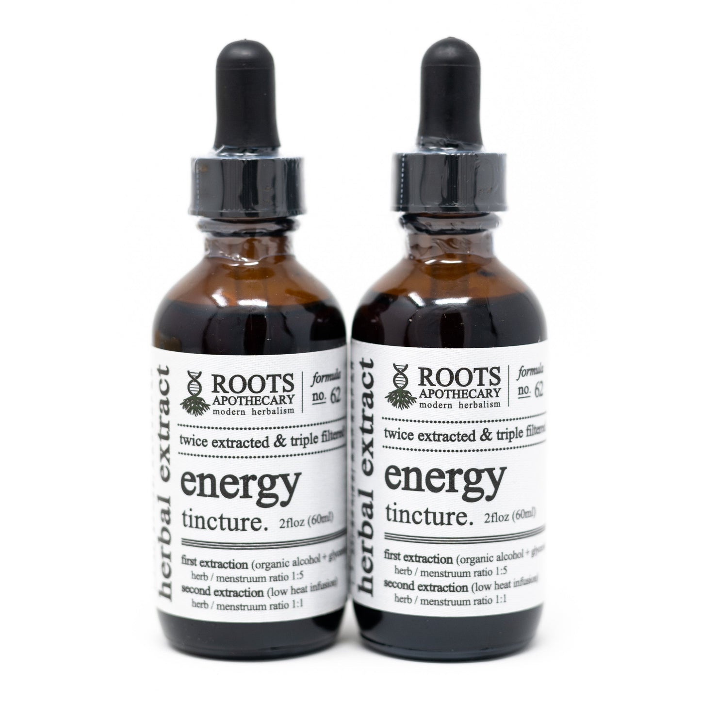 Two amber glass dropper bottles labeled Roots Apothecary energy tincture stand side by side, each with a black dropper cap and white label detailing herbal extracts, L-Theanine & Caffeine ingredients, and usage instructions.
