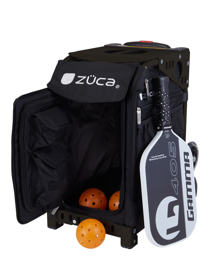 A ZUCA Pickleball Sport Black/Black rolling bag sits open, showing a roomy interior with three orange pickleballs inside. A white and black paddle is attached outside, while zippered compartments provide convenient storage for your gear.