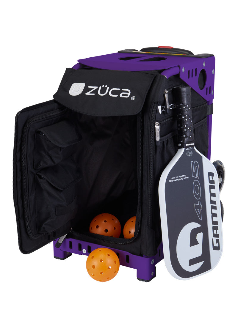 A ZUCA Pickleball Sport Black/Black rolling bag with an open front displays yellow pickleballs inside. A black-and-white Gamma G405 paddle attaches to the side. The bag includes wheels and multiple storage compartments for pickleballs.