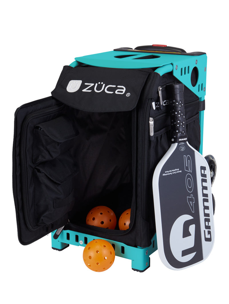 A ZUCA Pickleball Sport Black/Black rolling bag stands open, revealing three orange pickleballs inside. A black-and-white Gamma 405 paddle is attached; the bag features a soft zippered door and sturdy wheels for easy transport.