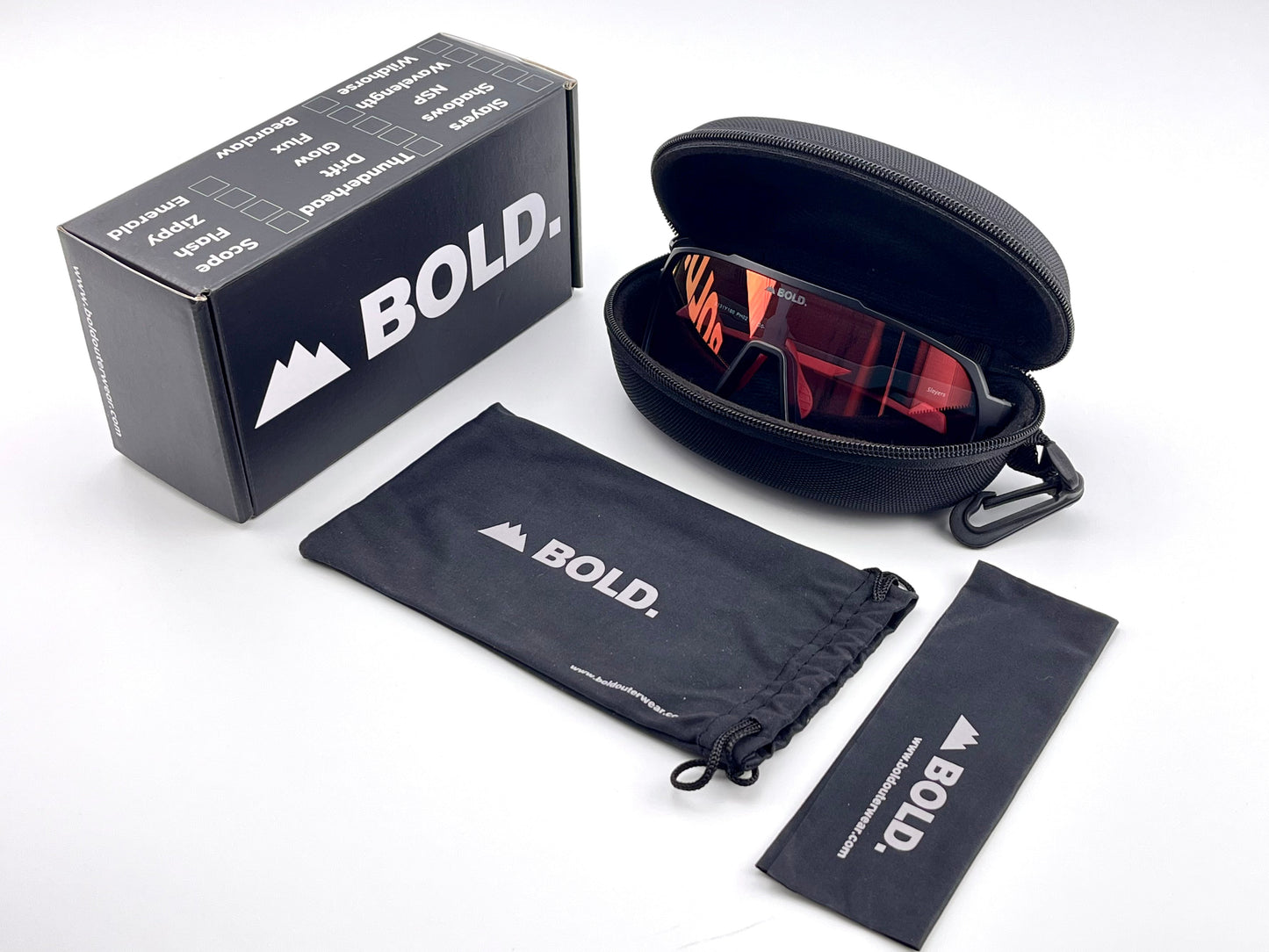 The BOLD Slayers Photochromic Sunglasses by boldouterwear are shown with an open hard case, black BOLD-branded box, soft pouch, and cleaning cloth on a white background. The red-lens sports sunglasses feature light-adaptive lenses.