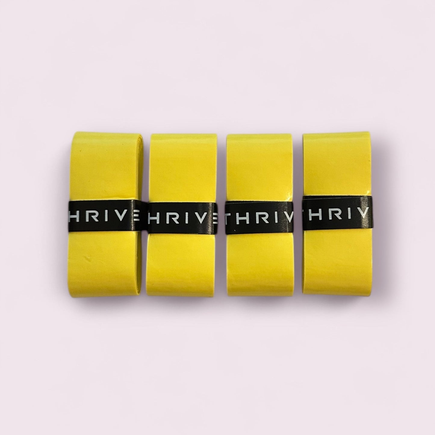 Four yellow Overgrips (Super Tacky) from Thrive Pickleball are arranged vertically on a light pink background, each held together by a black label with "THRIVE" in white uppercase letters.