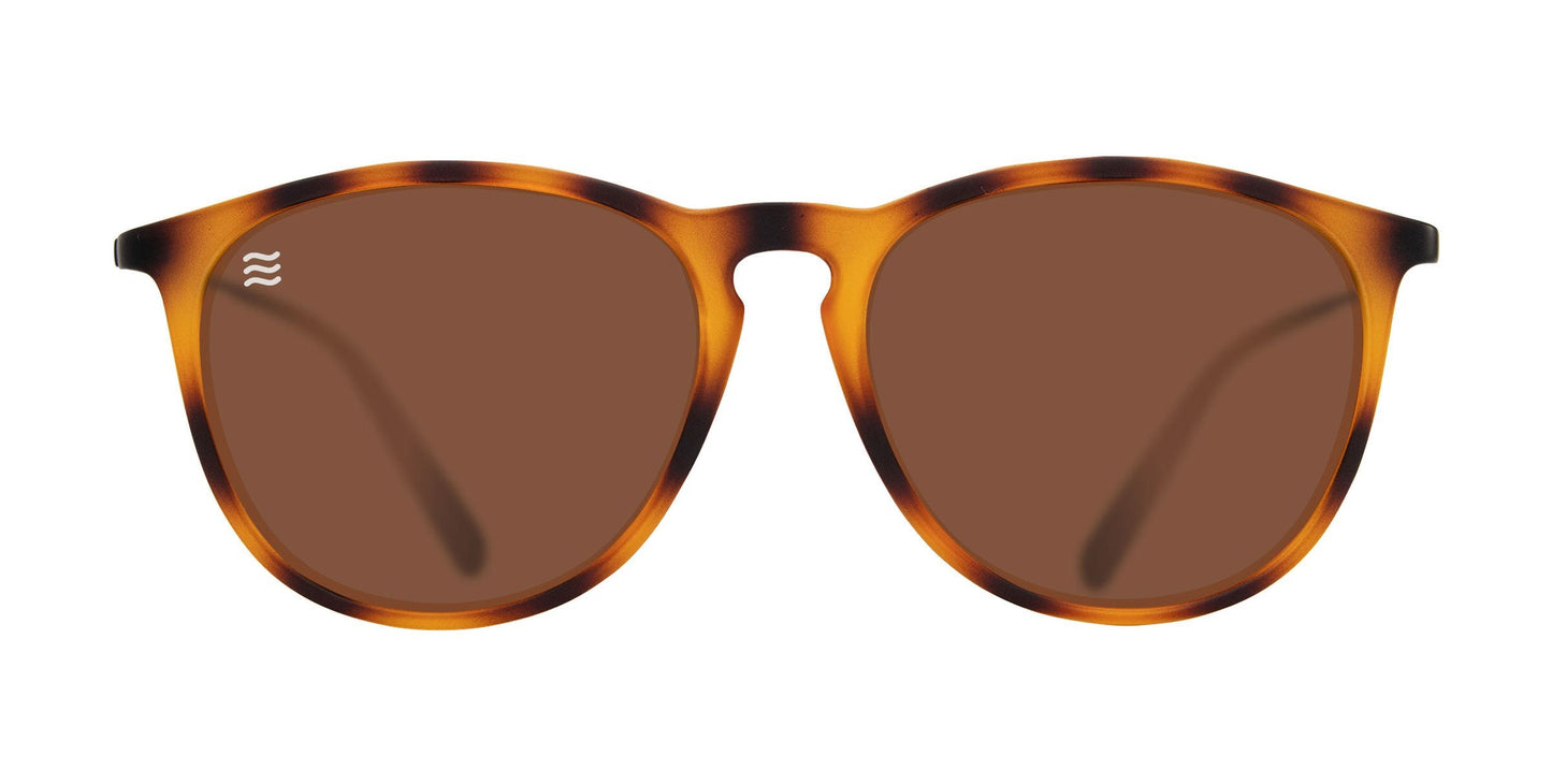 The Neven Eyewear Bowie sunglasses feature a tortoise TR90 frame with a mix of amber and dark brown, round brown-tinted lenses, and a small white wave logo on the upper left lens. The background is plain white.