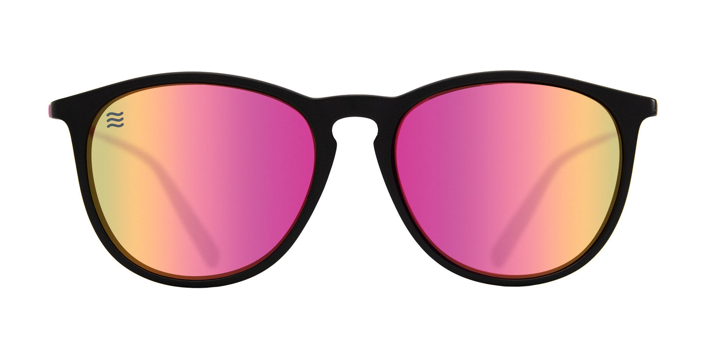 The Quinn sunglasses by Neven Eyewear feature black, round TR90 frames with pink-to-yellow mirrored polarized lenses. A small white wave logo appears on the top left lens. They are centered against a plain white background.