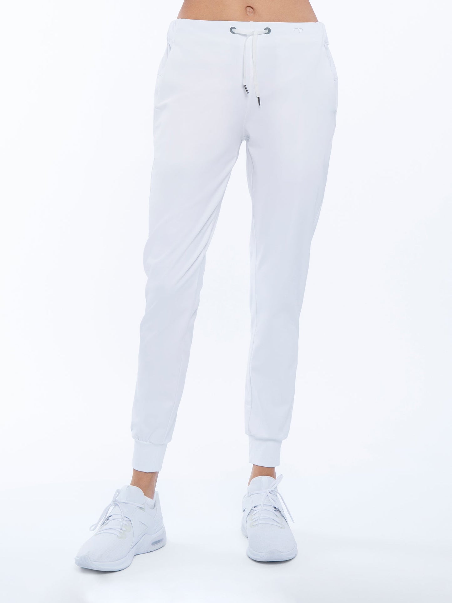 A person wears the Alexa Jogger - White by inPhorm NYC, featuring a drawstring waist, cuffed ankles, and UPF 50+ protection. Paired with white sneakers on a plain white background, only their legs and lower torso are seen.