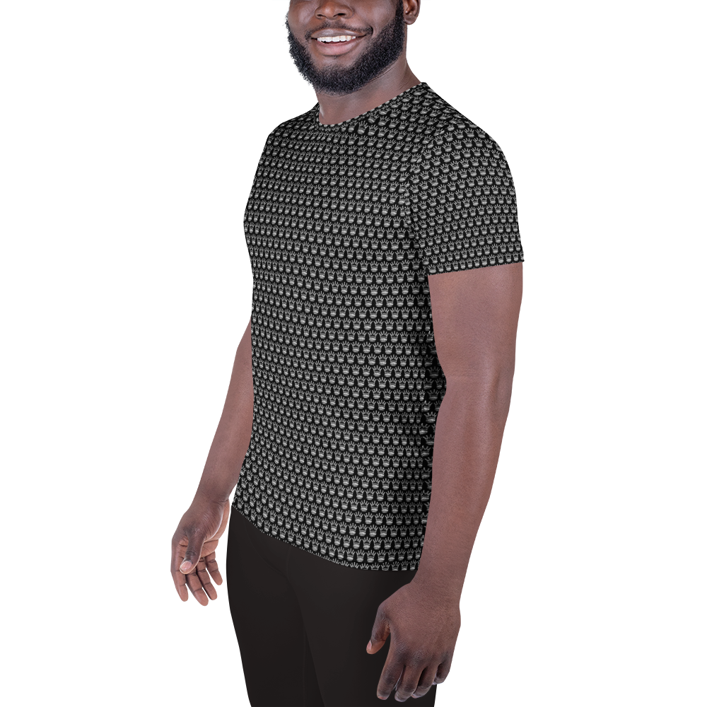 A smiling man with a short beard and mustache stands at a slight angle against a white background, wearing the Crown Pickleball Men's Corona Pattern Shirt in black with subtle gray and white geometric details, paired with black pants.