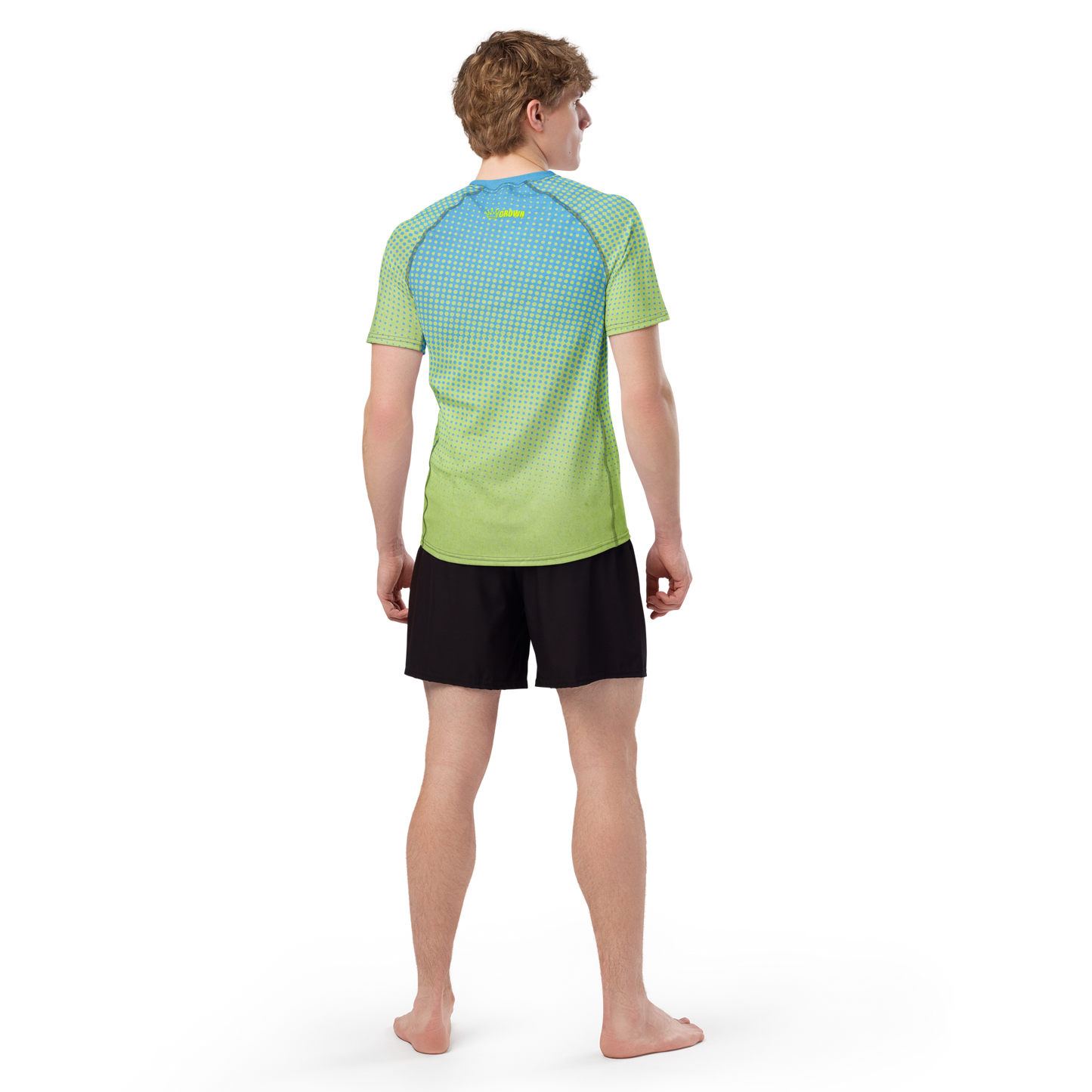 A person is standing barefoot, facing away, wearing the CROWN PICKLEBALL - Men's Tourney Shirt (Sea) by Crown Pickleball with black shorts. The background is plain white, and their arms rest naturally by their sides.