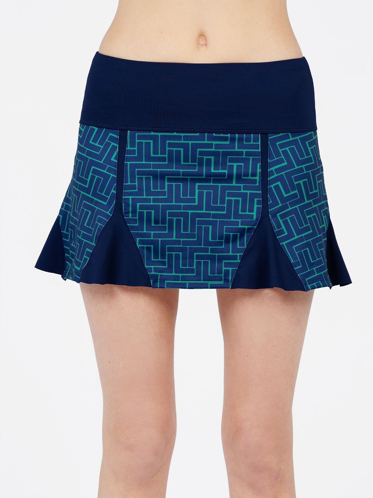 A woman wears the inPhorm NYC Alyssa A-Line Eco-Friendly Skort in Ink Tessel/Ink, featuring a navy waistband, flared navy side panels, and a geometric pattern on the front. Only her torso and upper legs are visible.