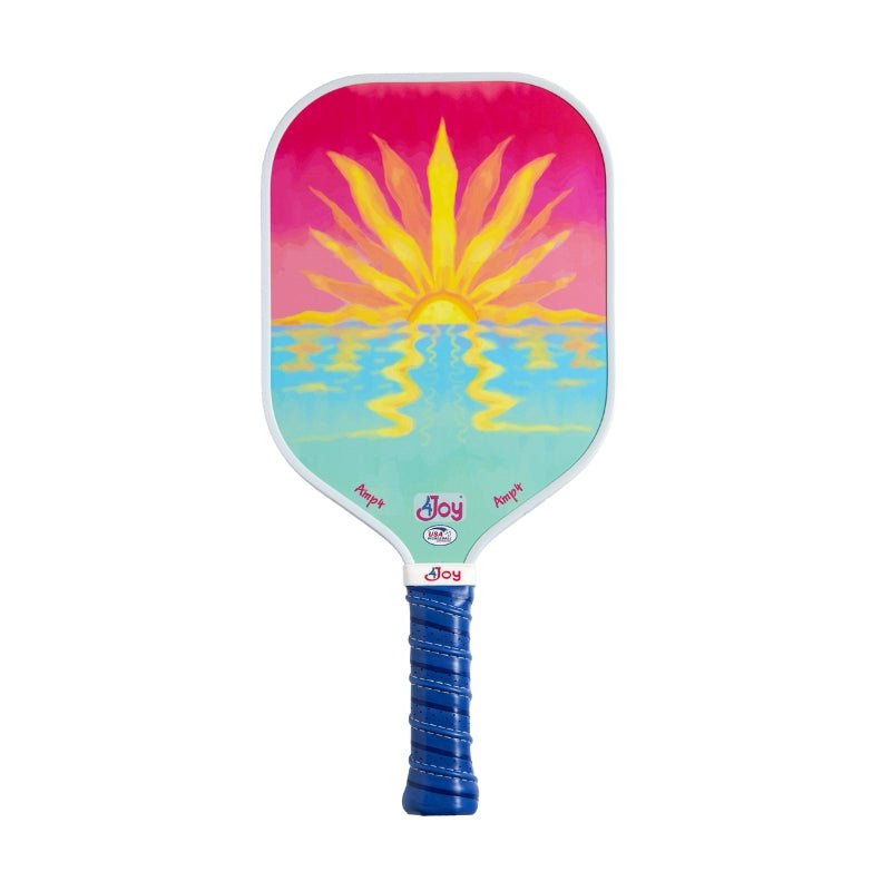 The 4Joy Paddles AMP4 Pickleball Paddle - Sunset features a dark blue grip, T700 carbon fiber face, and a vibrant yellow sun over blue water on a pink-orange sky. "Joy" is printed near the base of the paddle face.