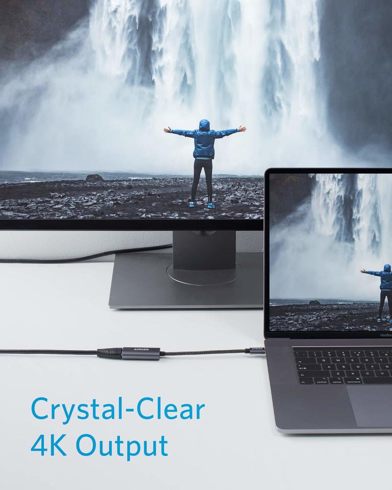 Anker 310 USB-C Adapter (4K HDMI) connects a laptop to a monitor, both showing a person in a blue jacket facing a waterfall. Text on screen: "Crystal-Clear 4K Output." Devices by Anker rest on a white surface.