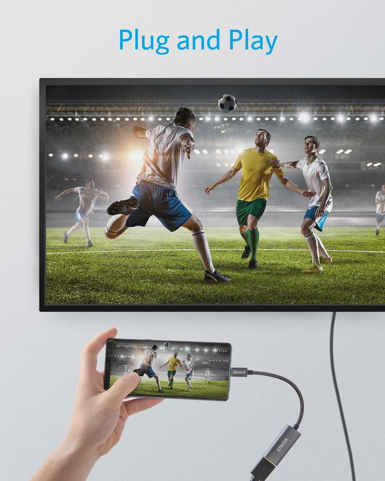 A hand streams a soccer match from a smartphone to a TV using the Anker 310 USB-C Adapter (4K HDMI). Both screens mirror the game in a lit stadium. Blue "Plug and Play" text appears above the TV against a plain white background.