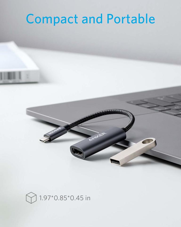 An Anker 310 USB-C Adapter (4K HDMI) with a short, flexible cable is plugged into a laptop. A metallic USB flash drive lies beside it. "Compact and Portable" appears above, with dimensions 1.97×0.85×0.45 in below.