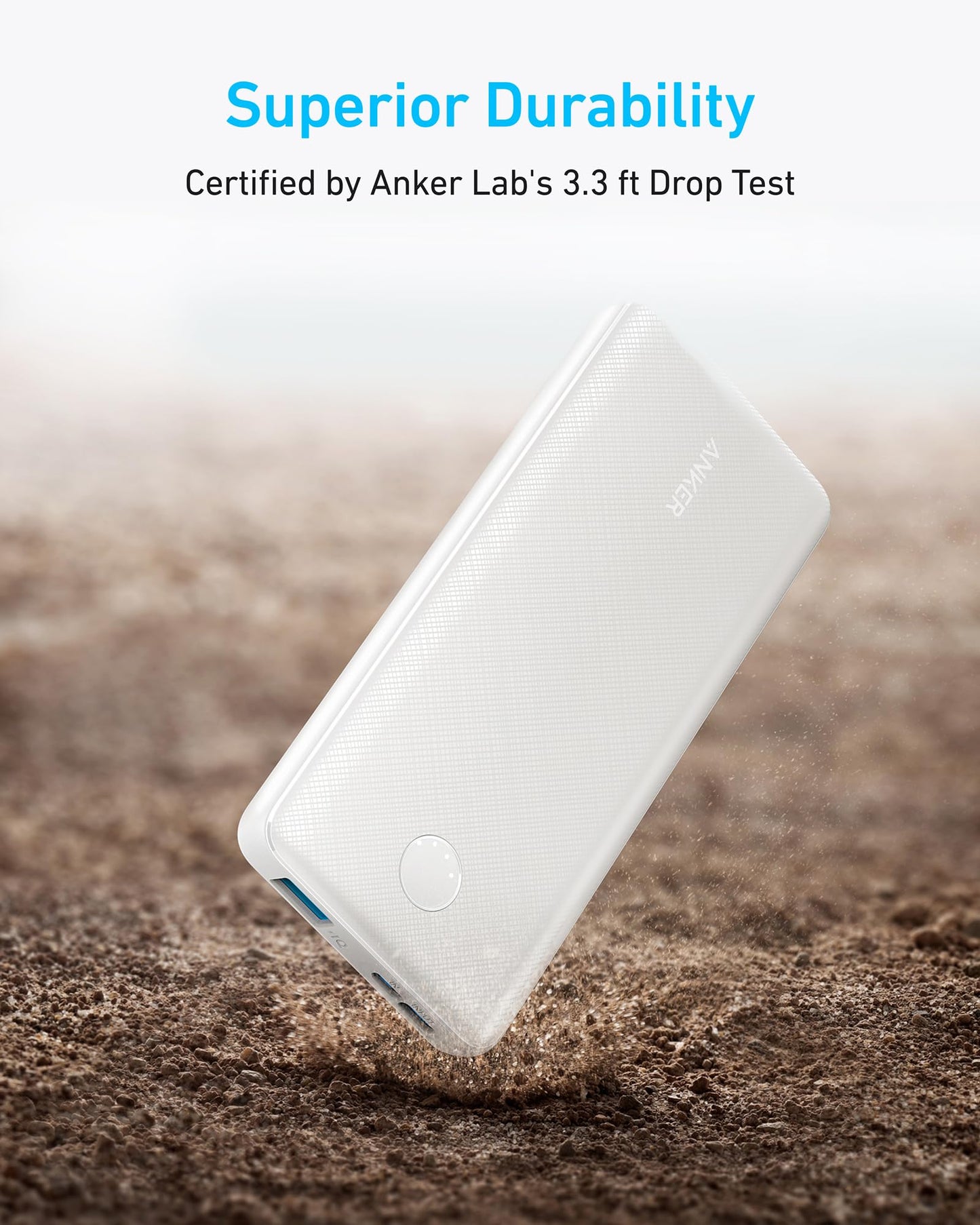 A white Anker 313 Power Bank (PowerCore 10K) rests on rough brown dirt as dust swirls around it. Above, text reads: Superior Durability Certified by Anker Labs 3.3 ft Drop Test, showcasing the product's toughness and resilience.