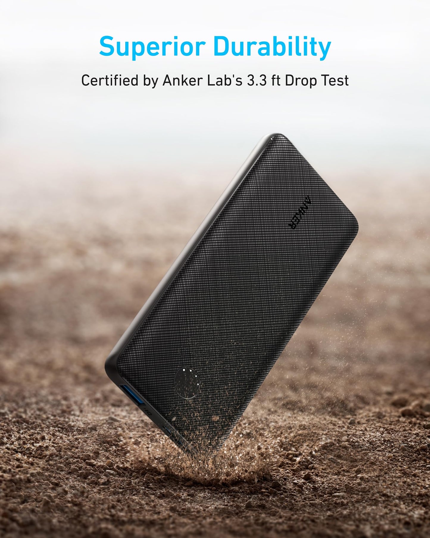 A black Anker <b>313</b> Power Bank (PowerCore 10K) is shown mid-air above rough ground, highlighting its durability. Text: "Superior Durability. Certified by Anker Lab’s 3.3 ft Drop Test." Scattered dust emphasizes impact resistance.