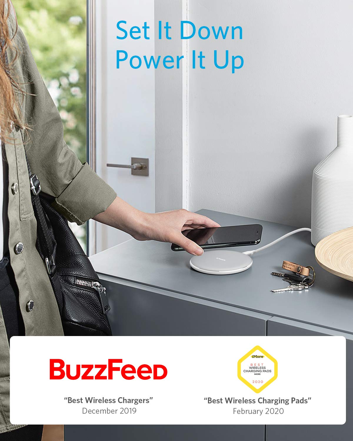A person places a smartphone on an Anker 313 Wireless Charger (Pad) by Anker on a gray counter. Above, "Set It Down Power It Up" is displayed. Decorative vases and wireless charging awards from BuzzFeed are seen below.