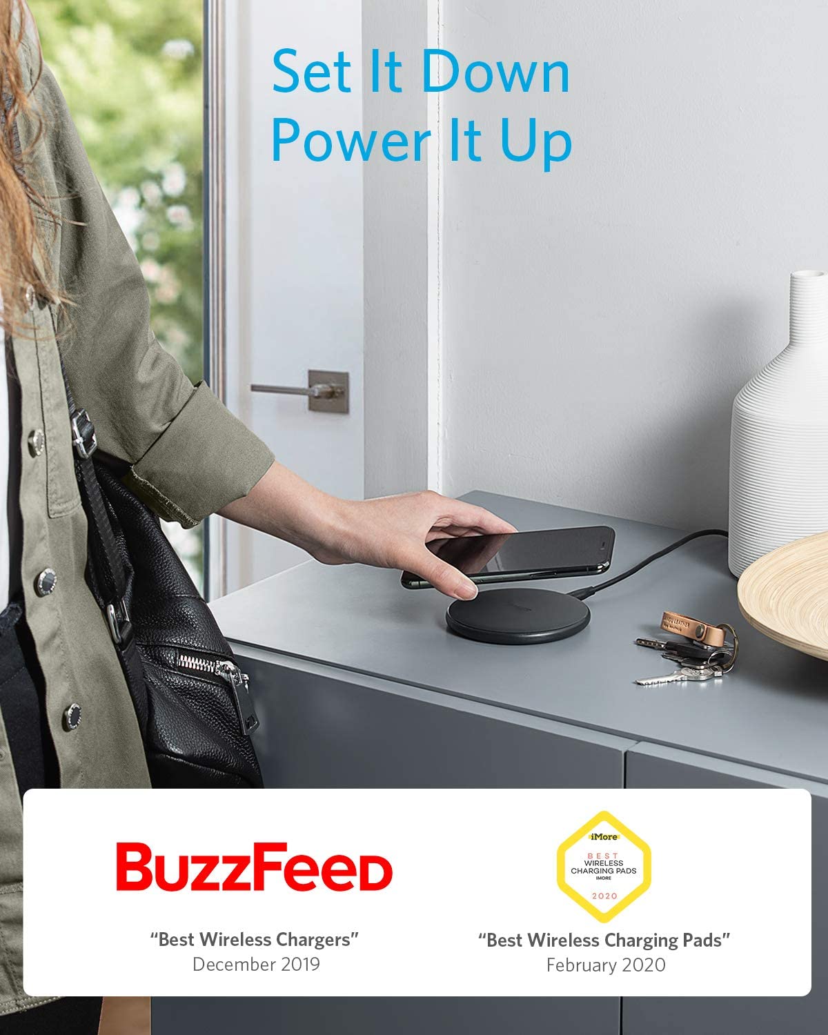 A person sets a smartphone on the Anker 313 Wireless Charger (Pad) by Anker, placed on a gray cabinet beside vases and a dish. Above is the text “Set It Down Power It Up,” with BuzzFeed and 2020 Best Wireless Chargers award logos below.