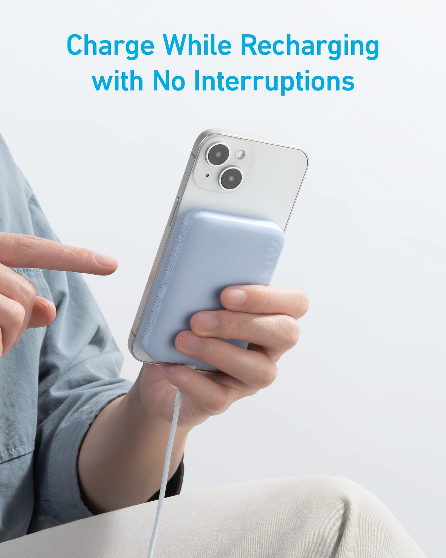 Someone holds a white phone with the Anker 321 MagGo Battery (PowerCore Magnetic 5K) attached and charging. A cable is connected while they point at the screen. Blue text above says: "Charge While Recharging with No Interruptions.
