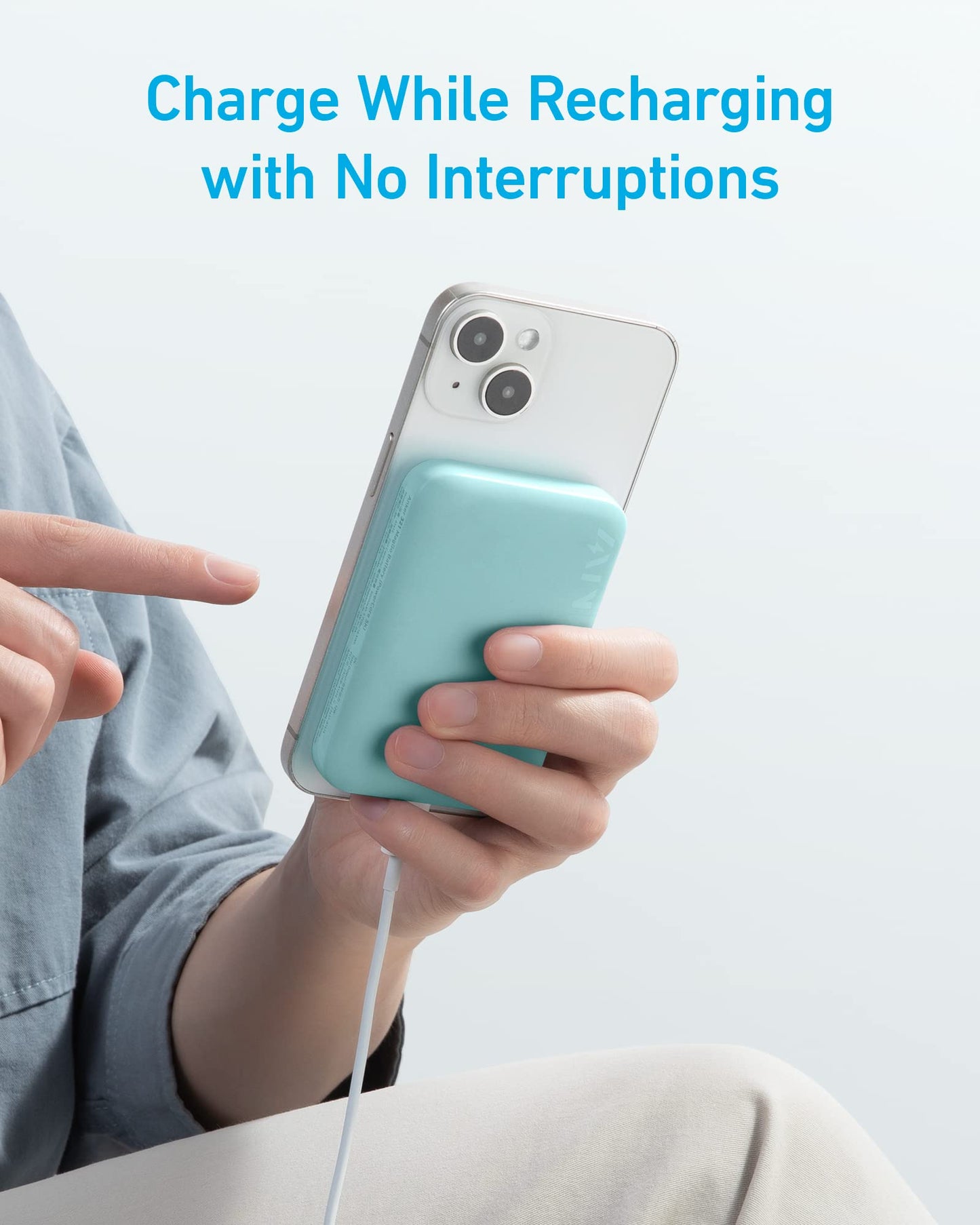 A person holds a white smartphone with the blue Anker 321 MagGo Battery (PowerCore Magnetic 5K) attached and charging via cable. Blue text above reads, "Charge While Recharging with No Interruptions." Light blue background.