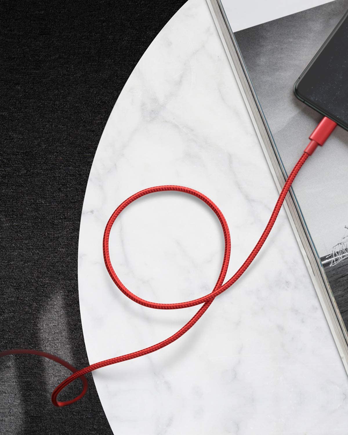 An Anker 331 USB-C to Lightning Cable connects a smartphone to a power source, lying in a loose loop on a white marble tabletop beside an open book, with only the phone and book corners visible. The table is set on a dark textured surface.