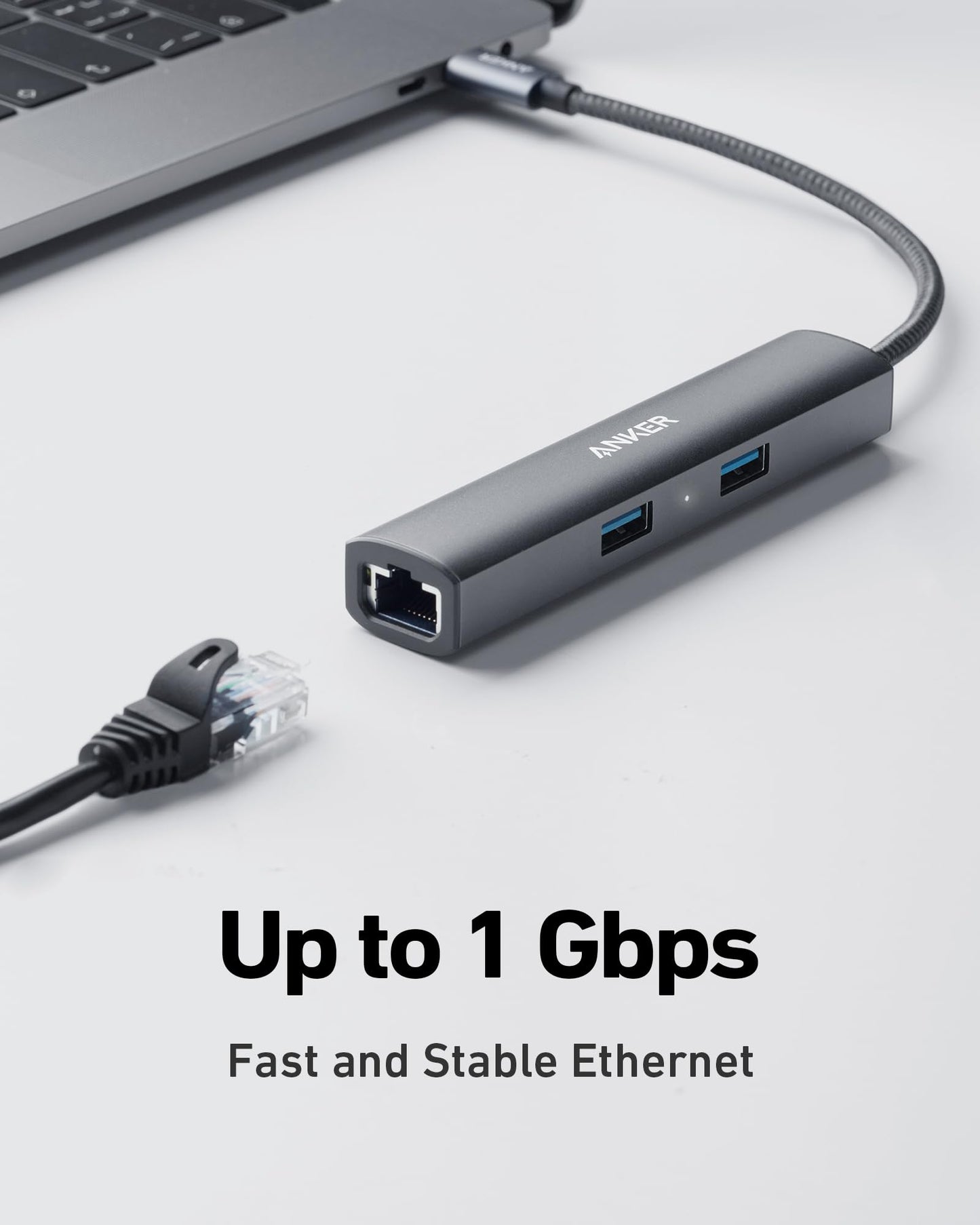 A close-up of the Anker 533 USB-C Hub (5-in-1, Slim) connected to a laptop, showing two USB ports, an HDMI port, and one Ethernet port. Ethernet cable nearby. Text: Up to 1 Gbps Fast and Stable Ethernet. Light gray background.