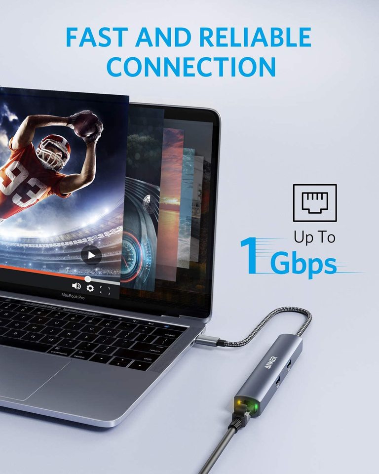 An Anker 543 USB-C Hub (6-in-1, Slim) in gray connects to a silver MacBook Pro with a braided cable. The screen shows a football video and "FAST AND RELIABLE CONNECTION" plus "Up To 1 Gbps" and an Ethernet Hub icon.
