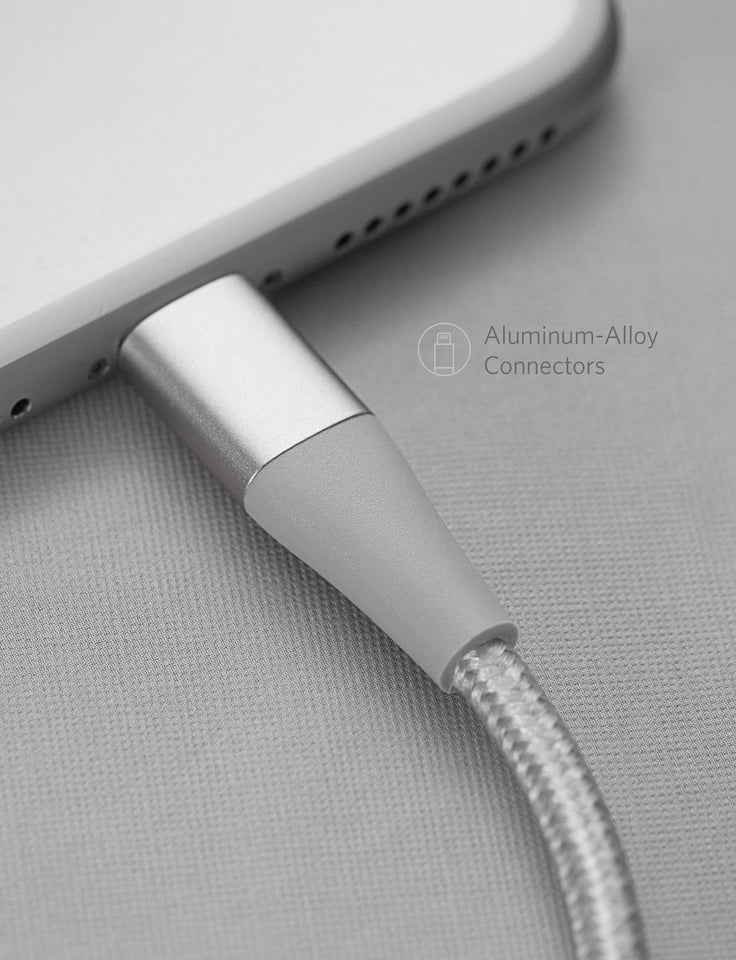 Close-up of an Anker 551 USB-A to Lightning Cable (10 ft) braided design, plugged into a smartphone with aluminum-alloy connector. Phone rests on a light textured surface. Text: Aluminum-Alloy Connectors with cable icon. Brand: Anker.
