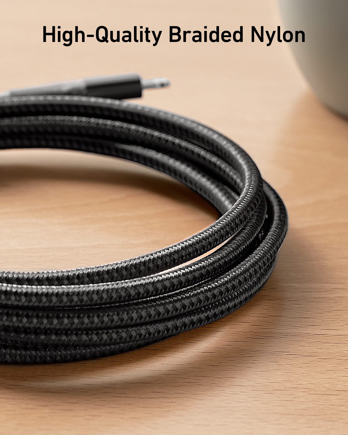 An Anker 551 USB-A to Lightning Cable (10 ft), black and coiled, lies on a light wooden surface. "High-Quality Braided Nylon" is shown above, with a white object partially visible in the top right corner.
