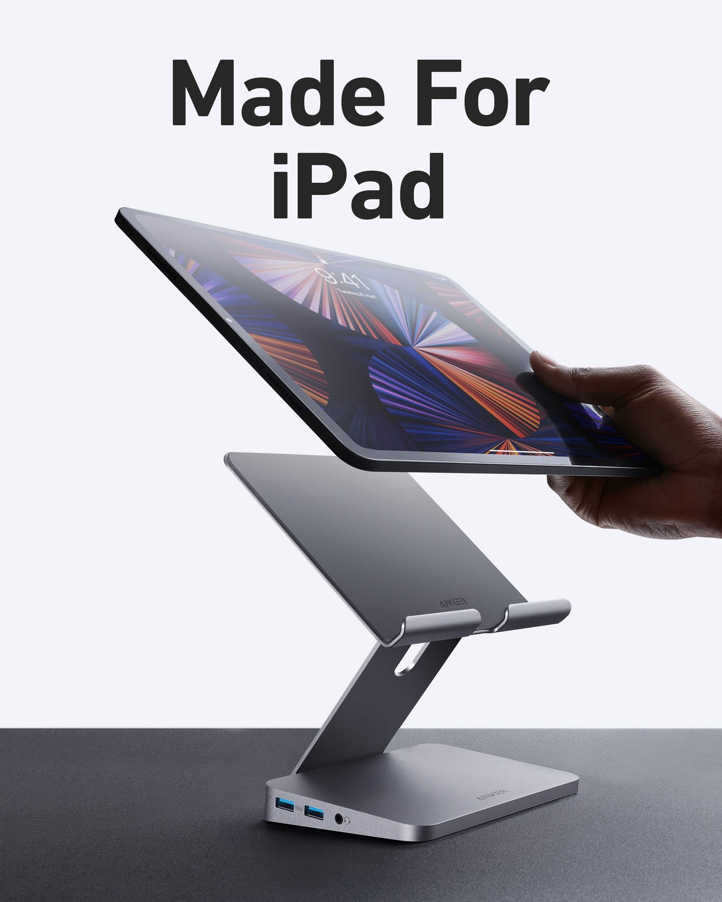 A hand sets a black iPad on the sleek, silver Anker <b>551</b> USB-C Hub (8-in-1, Tablet Stand) with HDMI and multiple USB ports. "Made For iPad" appears above. The light gray background highlights this versatile docking station.