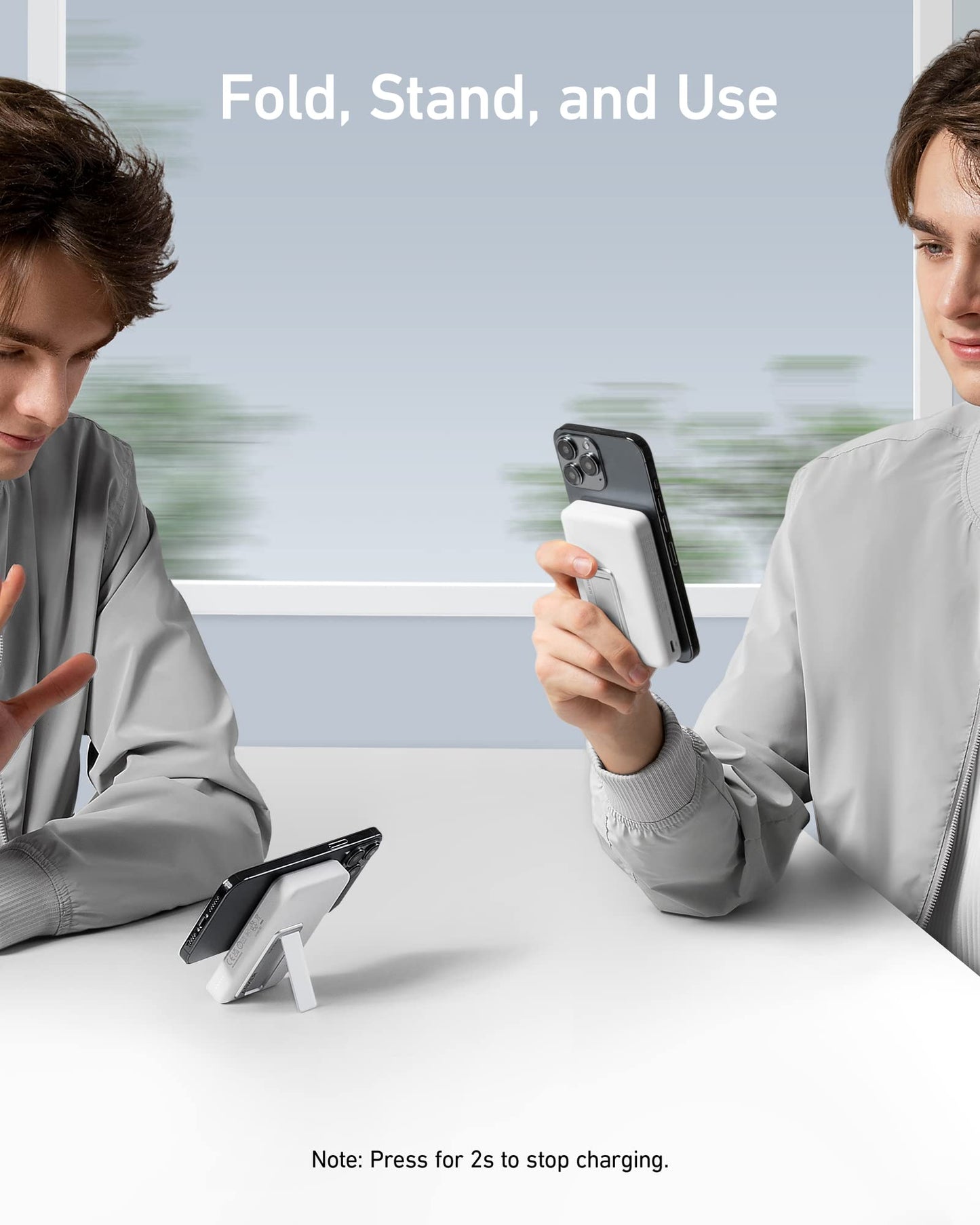 Two young men in gray jackets sit at a table. One holds a smartphone with the white Anker 633 Magnetic Battery wireless charger and folding stand; the other gestures to another phone on the same versatile Anker stand. "Fold, Stand, and Use" appears above.