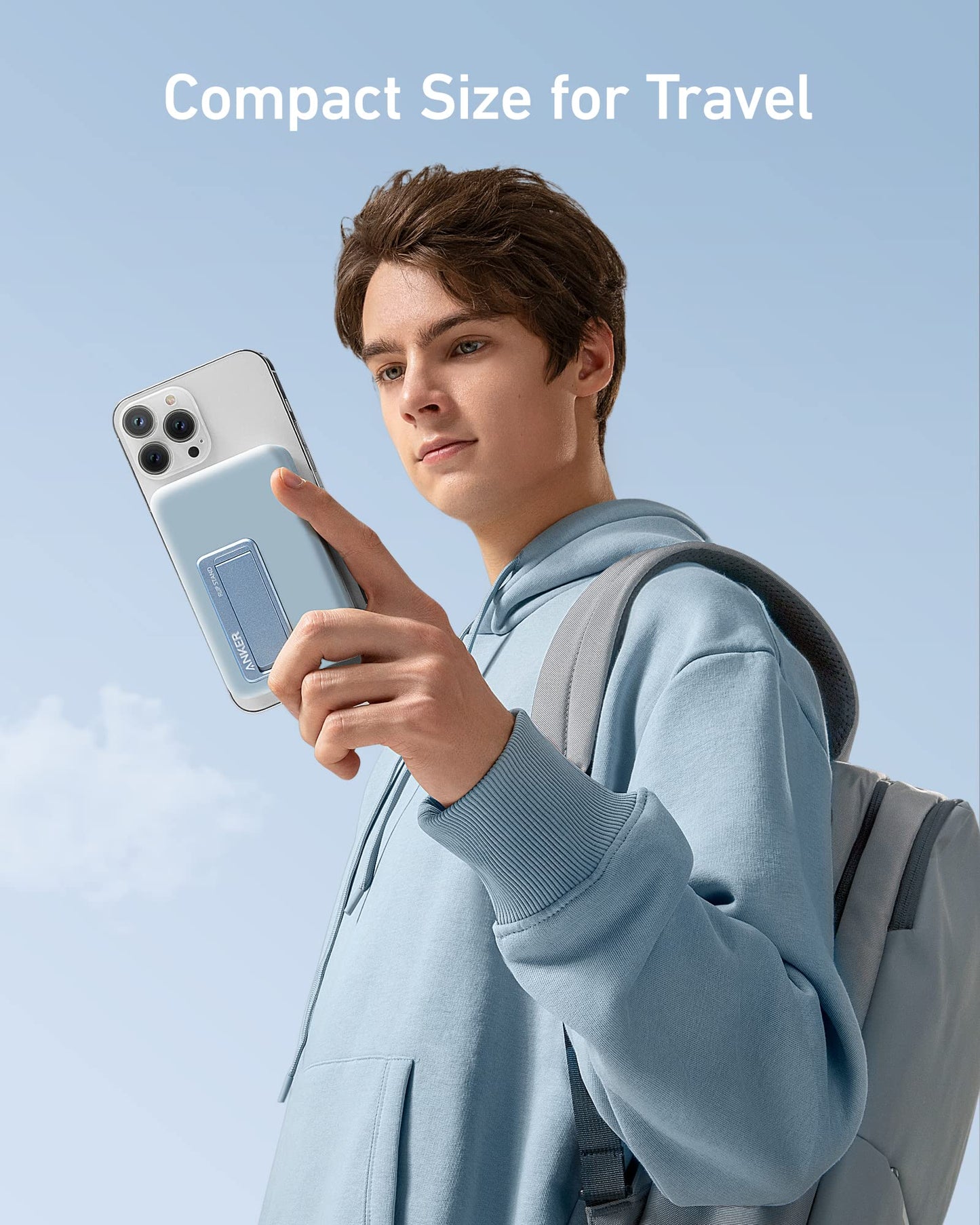 A young person in a blue hoodie and gray backpack holds a smartphone with an Anker 633 Magnetic Battery by Anker, featuring a sleek blue card holder. The clear blue sky background has white text: “Compact Size for Travel.”.