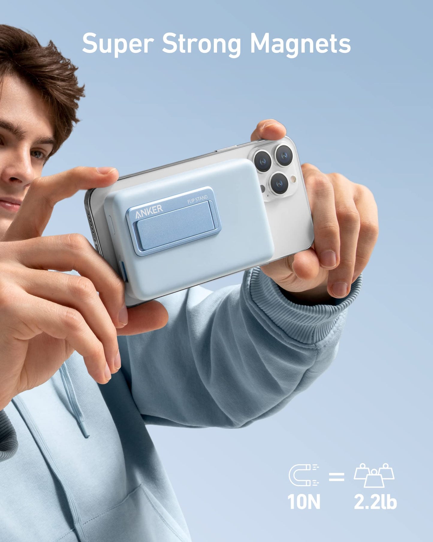 A person in a light blue hoodie attaches the Anker 633 Magnetic Battery to a silver smartphone. Above, “Super Strong Magnets” is displayed, with an icon showing “10N = 2.2lb,” highlighting the wireless charger’s holding power.