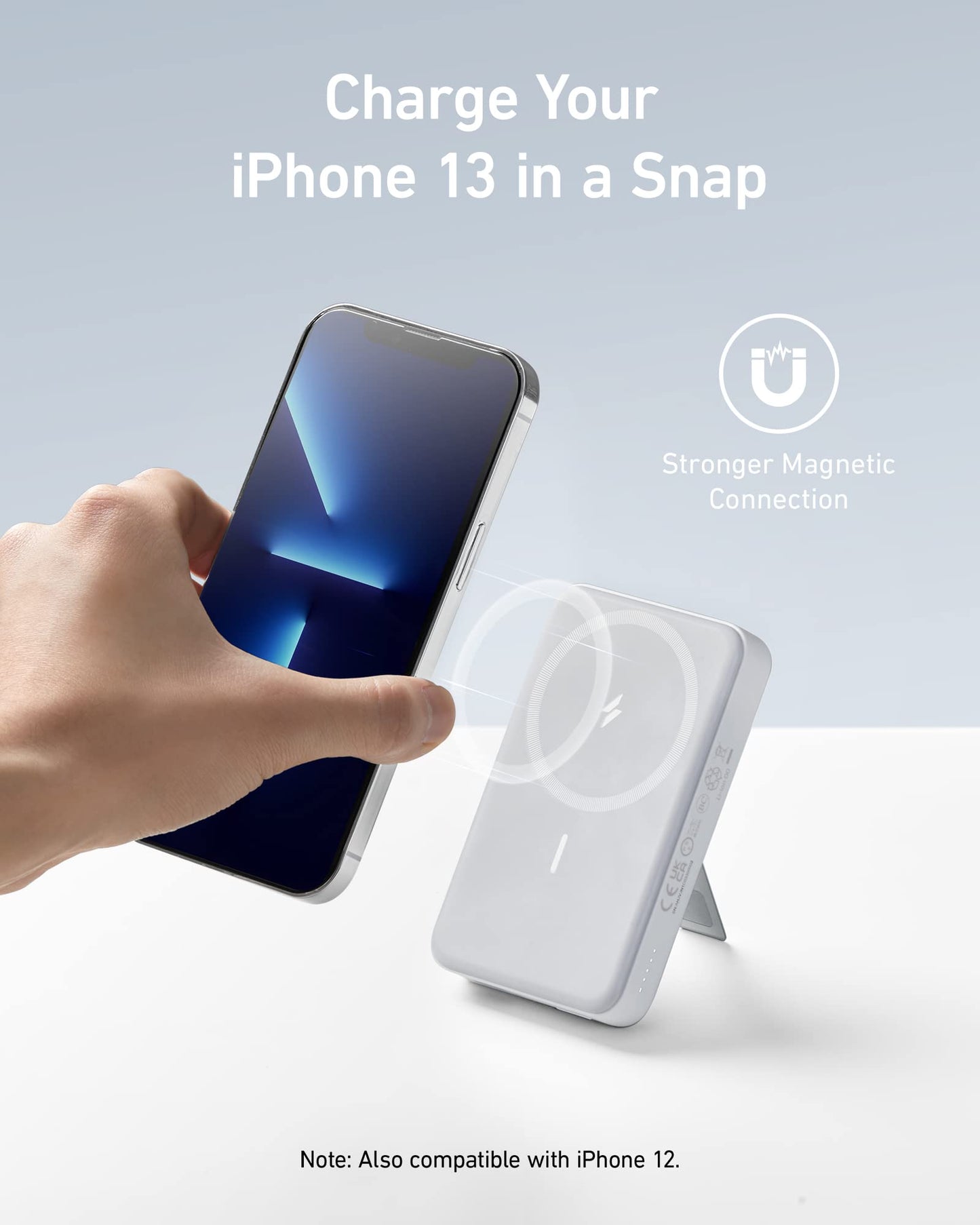 A hand holds an iPhone 13 near the white Anker 633 Magnetic Battery on a stand. Text above reads: Snap and Charge Your iPhone 13 with Strong Anker Magnetic Connection. Compatible and pairs with a 10,000mAh battery for extra power.