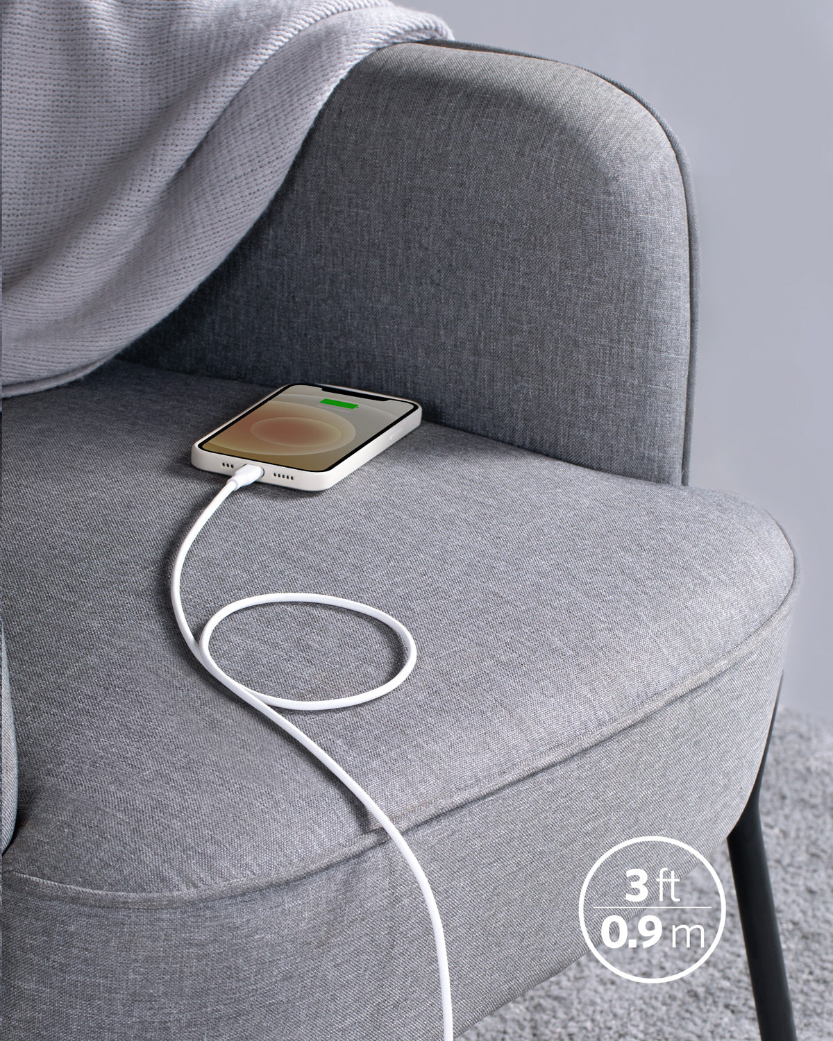 A smartphone charges on a light grey chair using the Anker 641 USB-C to Lightning Cable (Flow, 3 ft Silicone), an MFi certified cable. The phone displays a partially charged battery. A soft blanket is draped over the chair.