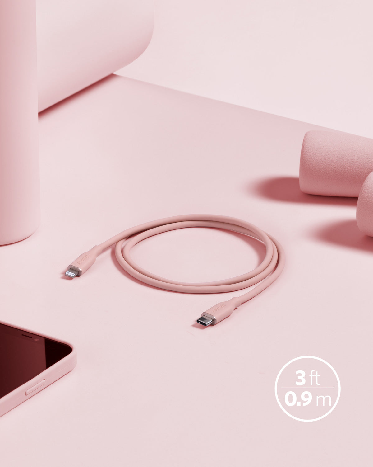 The Anker 641 USB-C to Lightning Cable (Flow, 3 ft Silicone) is coiled on a light pink surface, surrounded by pink items—a smartphone, bottle, and dumbbell—creating a stylish monochromatic look. “3 ft 0.9 m” marks its length. Brand: Anker.