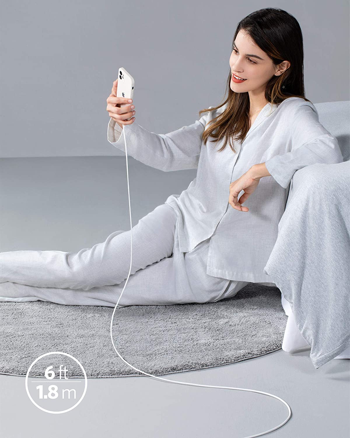 A woman in light gray pajamas sits on a rug, smiling as she holds her smartphone with the Anker 641 USB-C to Lightning Cable (Flow, 3 ft Silicone), highlighted by “3 ft” in a white circle on the rug. The cable is MFi certified by Anker.