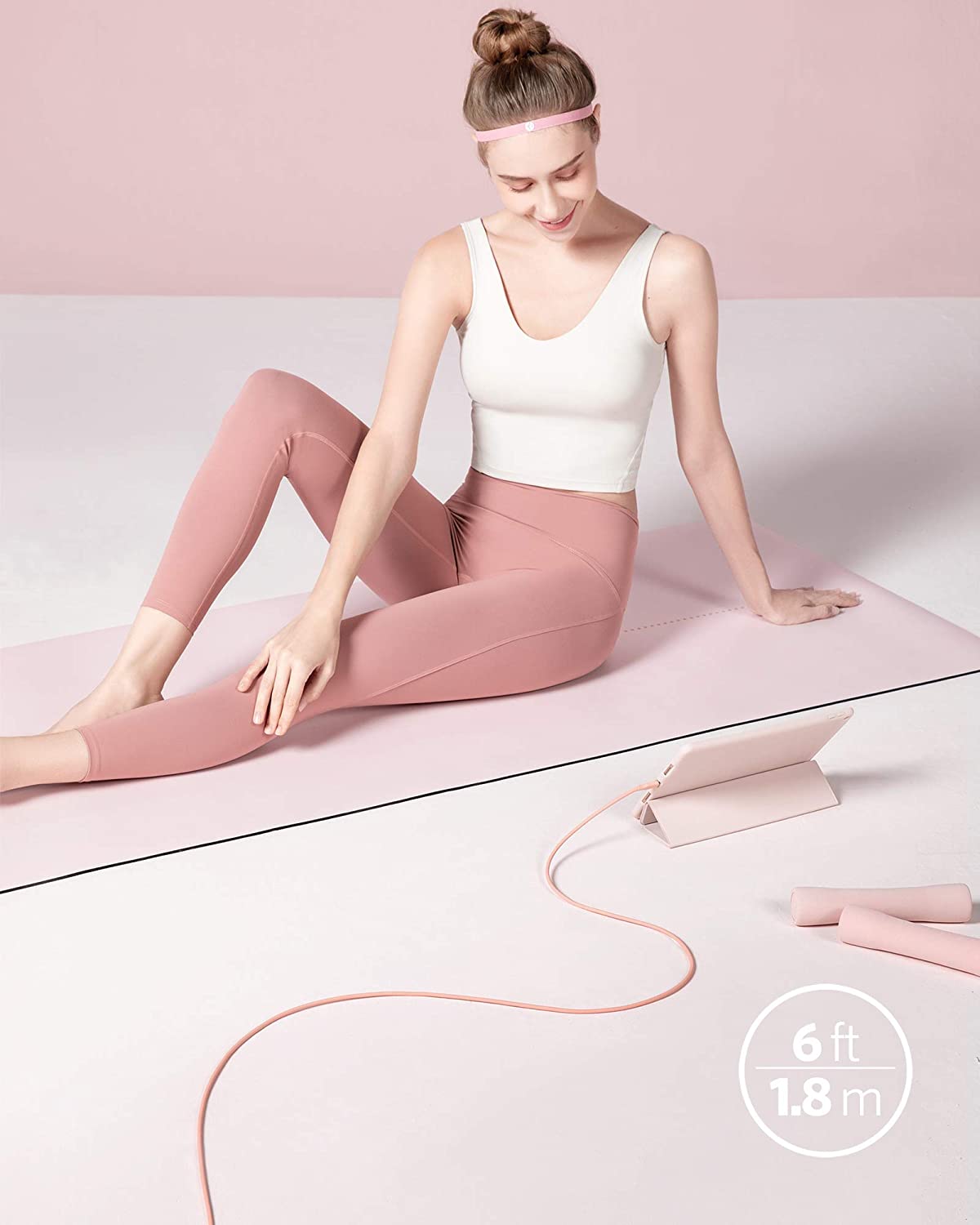 A woman in a white tank top and pink leggings sits on a pink yoga mat, smiling at a tablet. Beside her are a pink jump rope with case and an Anker 641 USB-C to Lightning Cable (Flow, 3 ft Silicone). The background and floor are pink; text reads 6 ft 1.8 m.