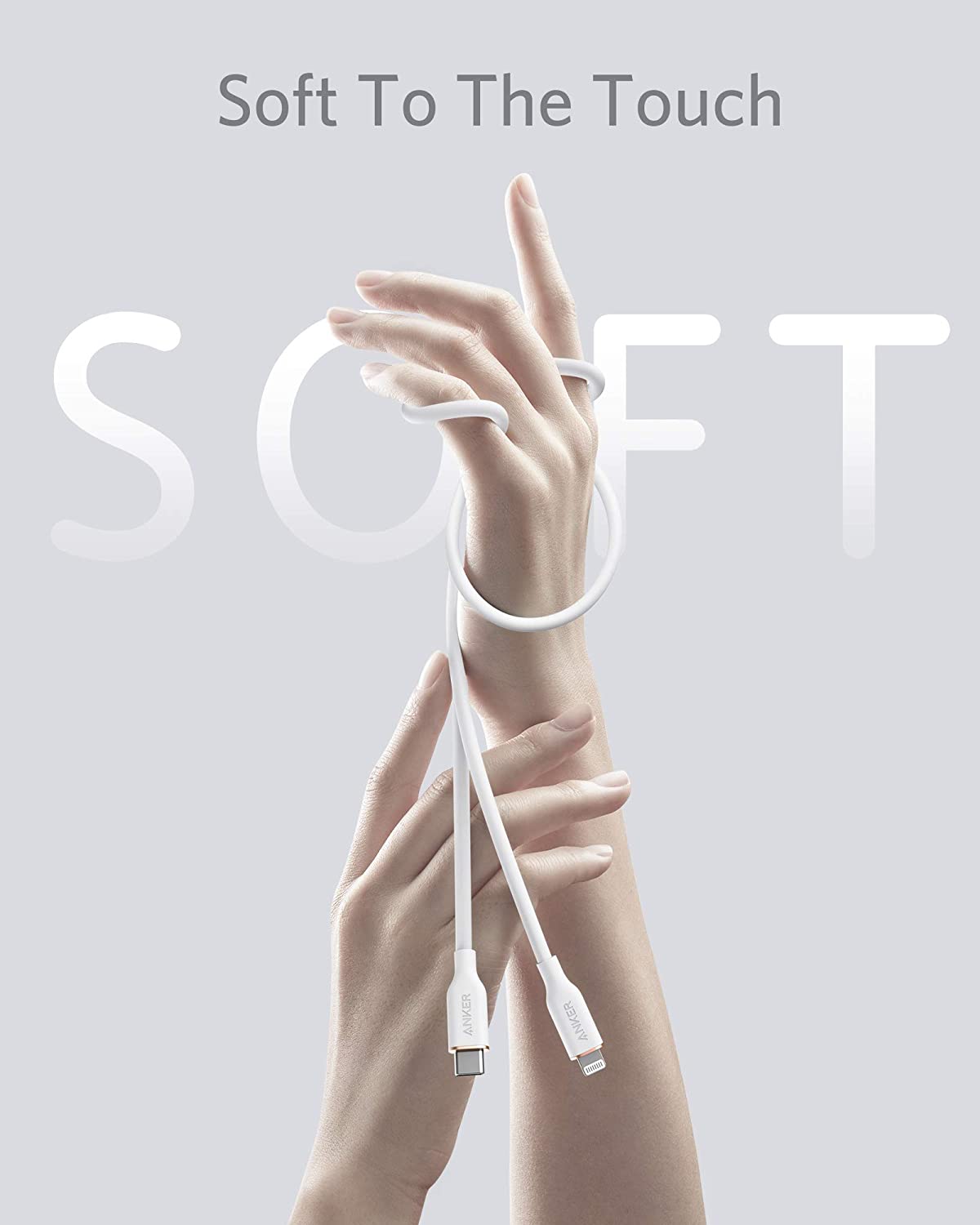 A white Anker 641 USB-C to Lightning Cable (Flow, 3 ft Silicone) is loosely wrapped around two elegantly posed hands against a pale gray background. Large, semi-transparent letters spell SOFT above the phrase "Soft To The Touch," creating a clean, minimalistic look.