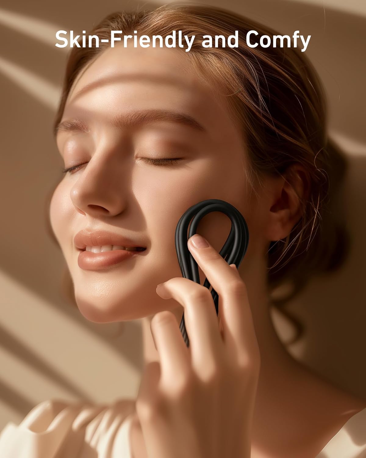 A young woman with fair skin smiles gently while using the black, loop-shaped Anker 643 USB-C to USB-C Cable (Flow, Silicone). Soft sunlight falls on her face. The text Skin-Friendly and Comfy appears above, highlighting fast charging ease.