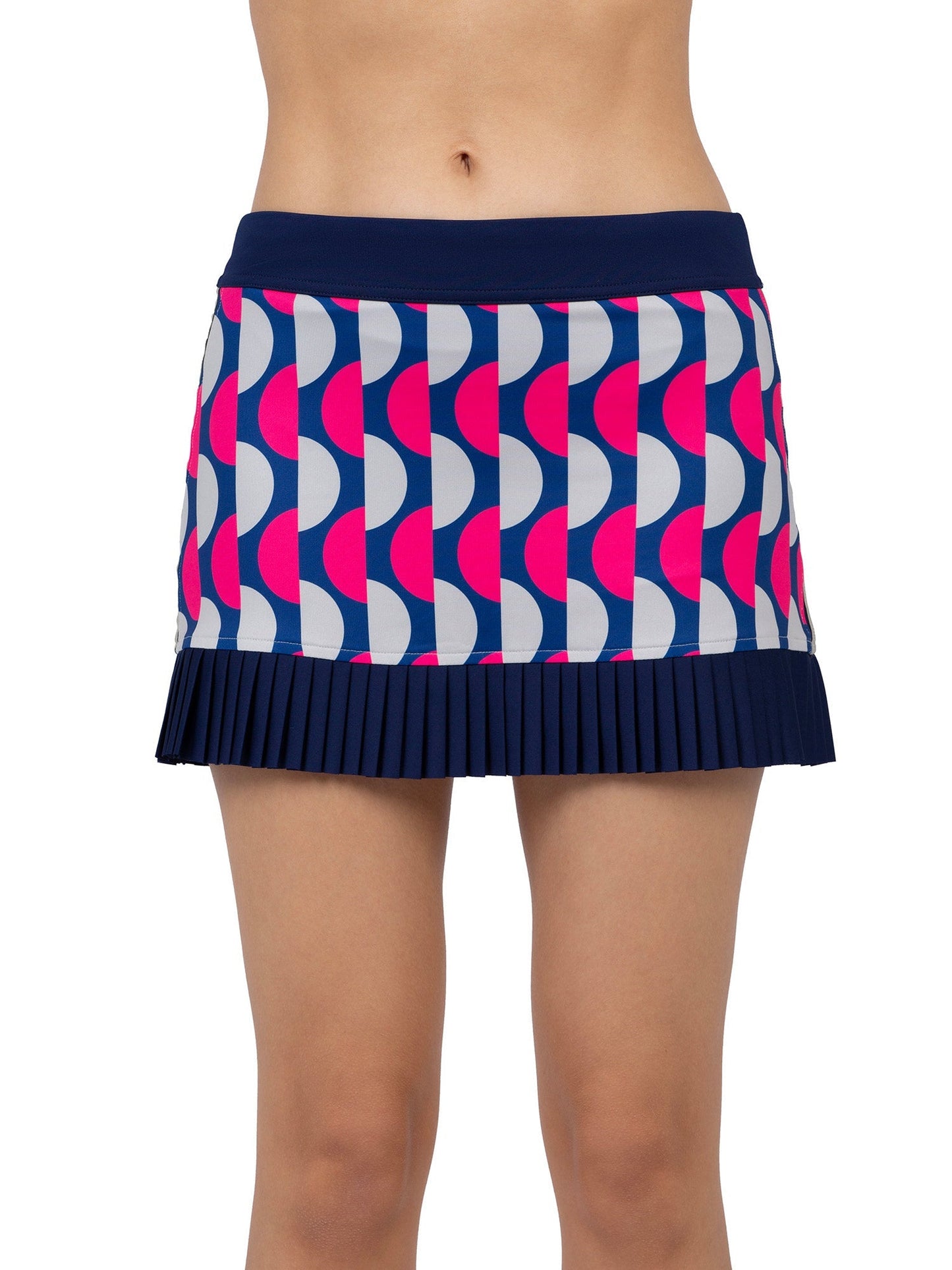 A person models the inPhorm NYC Audrey Tennis & Pickleball Skirt, a high-waisted design with vertical pleats at the hem and a bold geometric pattern in navy, white, and pink. Only the torso and legs show against a plain white background.