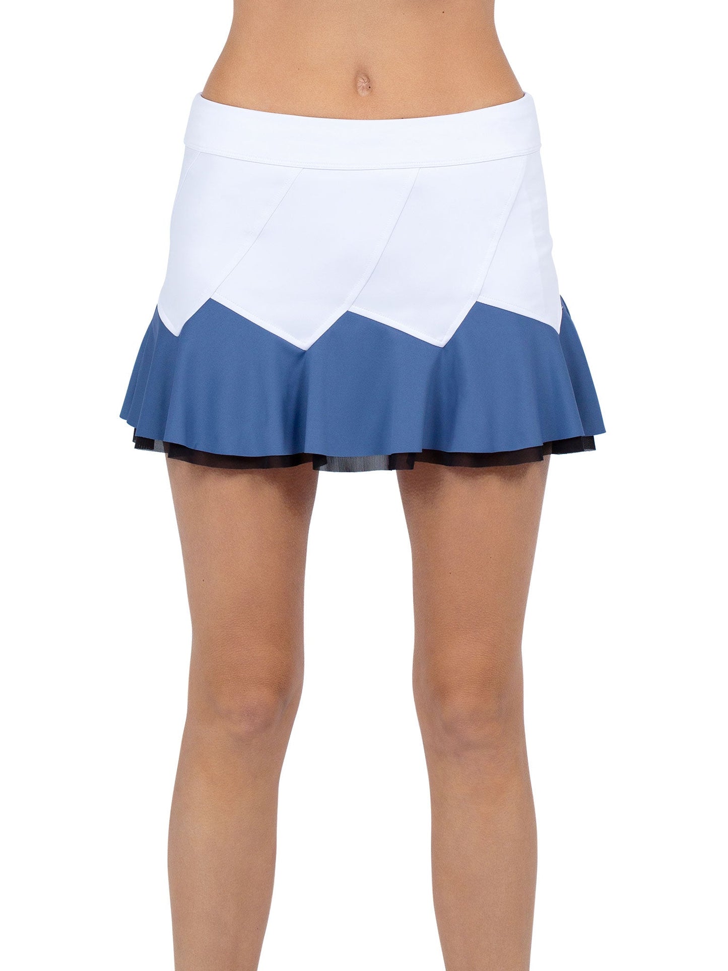 A person models the inPhorm NYC Baseline Butterfly Skirt - White/Palladian Combo, featuring a white top, blue bottom, geometric panels, and flared ruffled hem. The performance fabric skirt highlights the midriff and legs against a plain white background.