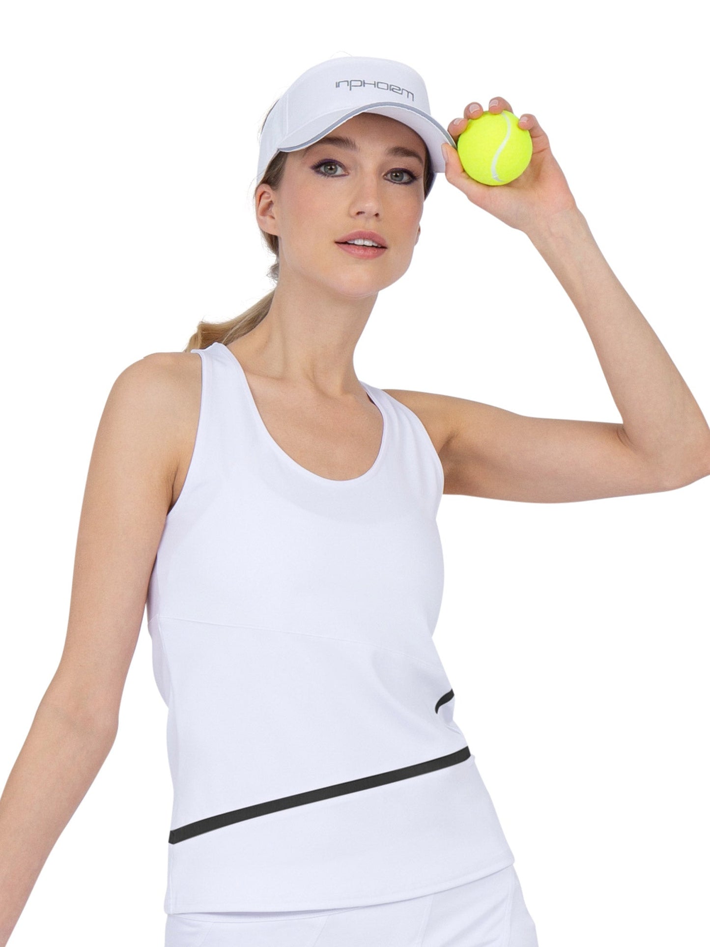A woman with blond hair in a ponytail and blue eyes wears the inPhorm NYC Baseline Tank - White/Black and visor, holding a yellow tennis ball near her head. The plain white background highlights her athletic pickleball style.