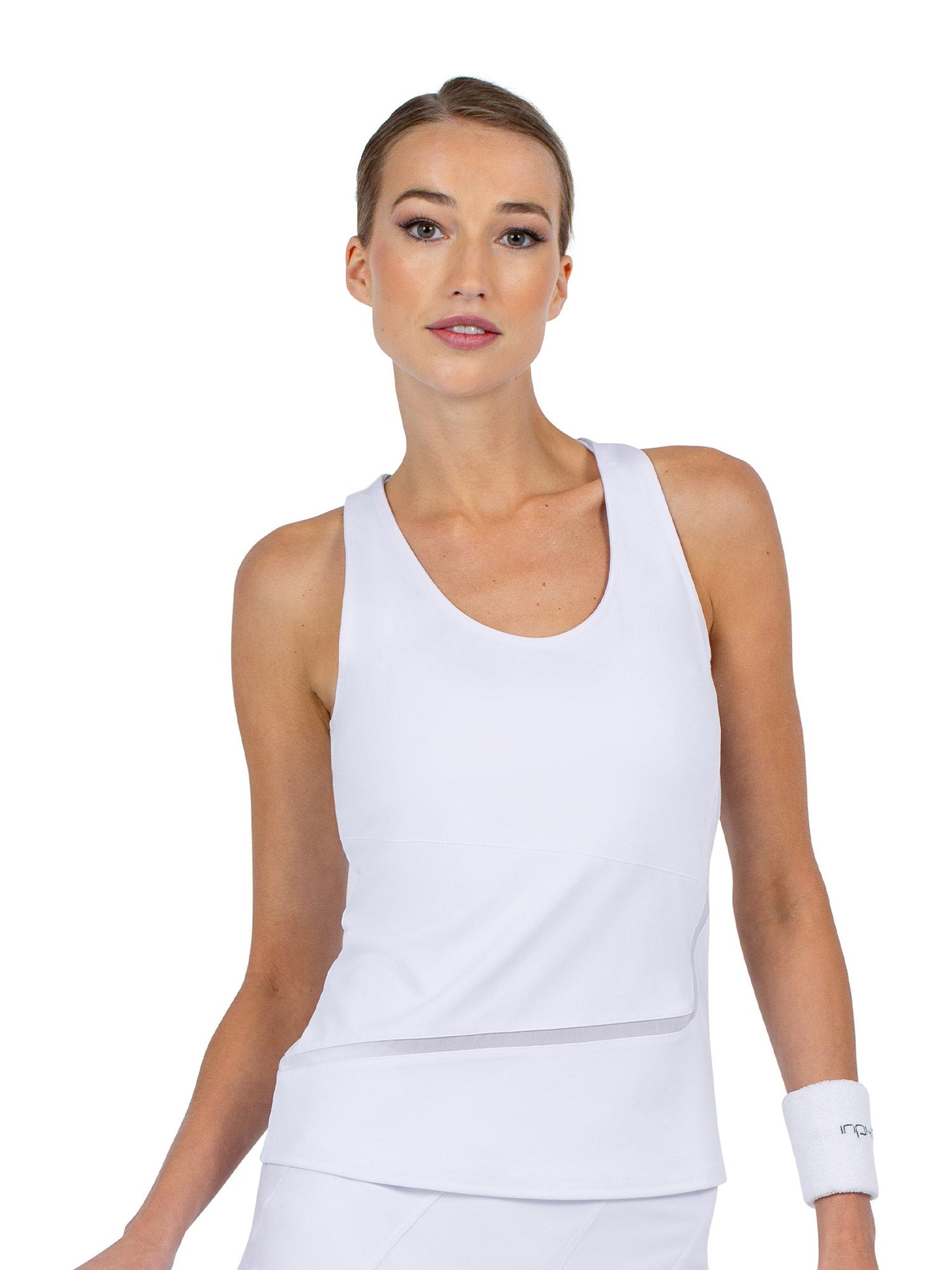 A woman with light skin and blond hair pulled back wears the inPhorm NYC Baseline Tank in white, along with a matching wristband. She stands against a plain white background, looking forward with a neutral expression.