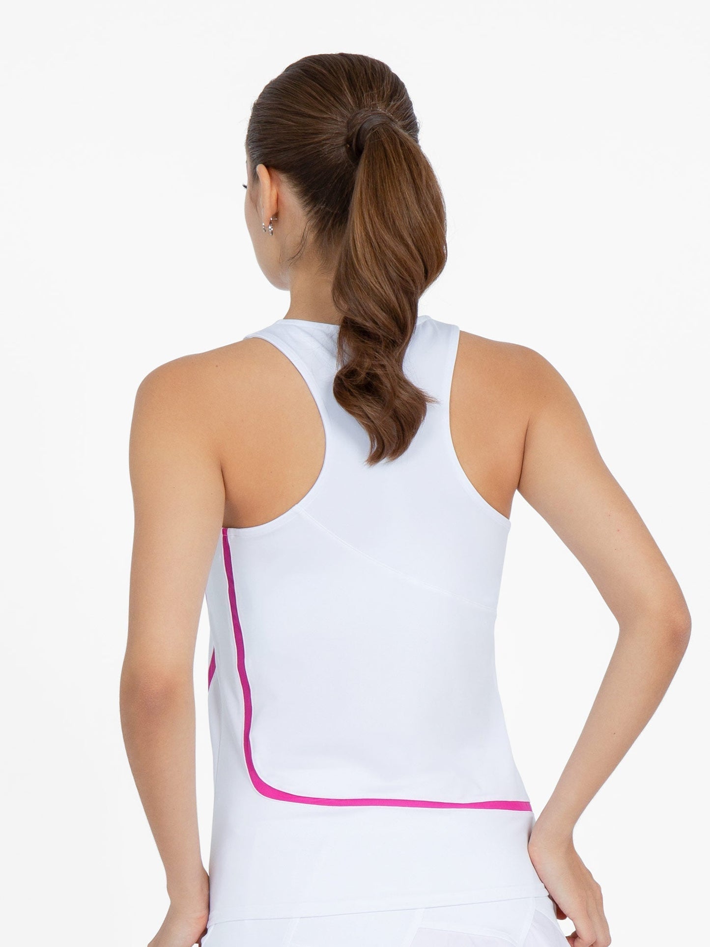 A woman with brown hair in a ponytail is shown from the back wearing the inPhorm NYC Baseline Tank - White/Pink. Her right hand rests on her hip against a plain white background.