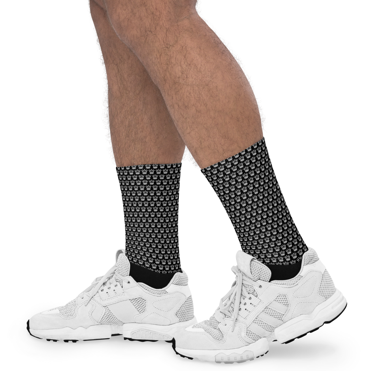 A person wears CROWN PICKLEBALL - Checkered Crown (Black) socks by Crown Pickleball with white sneakers, standing on a white background. Only the lower legs and feet are visible, showcasing the socks’ checkered crown design.