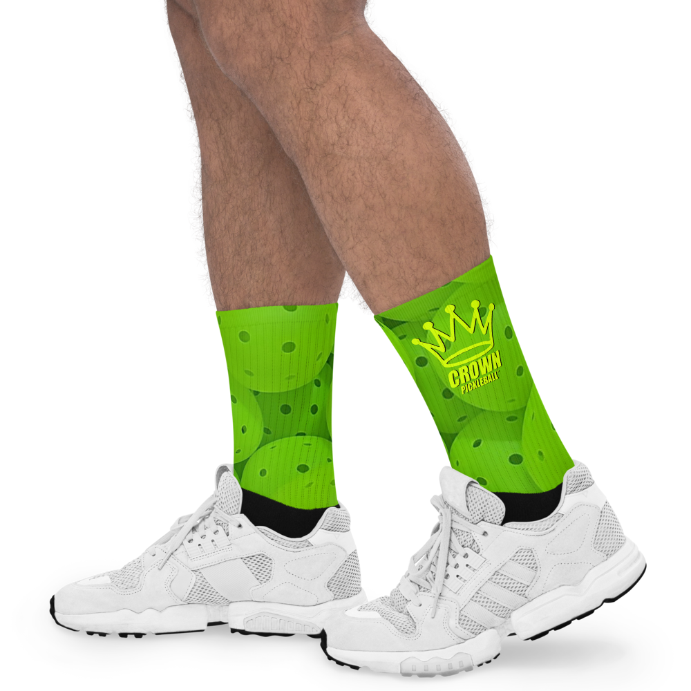 A person sports Crown Pickleball’s bright green Performance Athletic Crew Socks for Pickleball Players, featuring a yellow crown and “CROWN PICKLEBALL” in bold, with subtle dot patterns, paired with white athletic sneakers. Only legs and feet are shown.