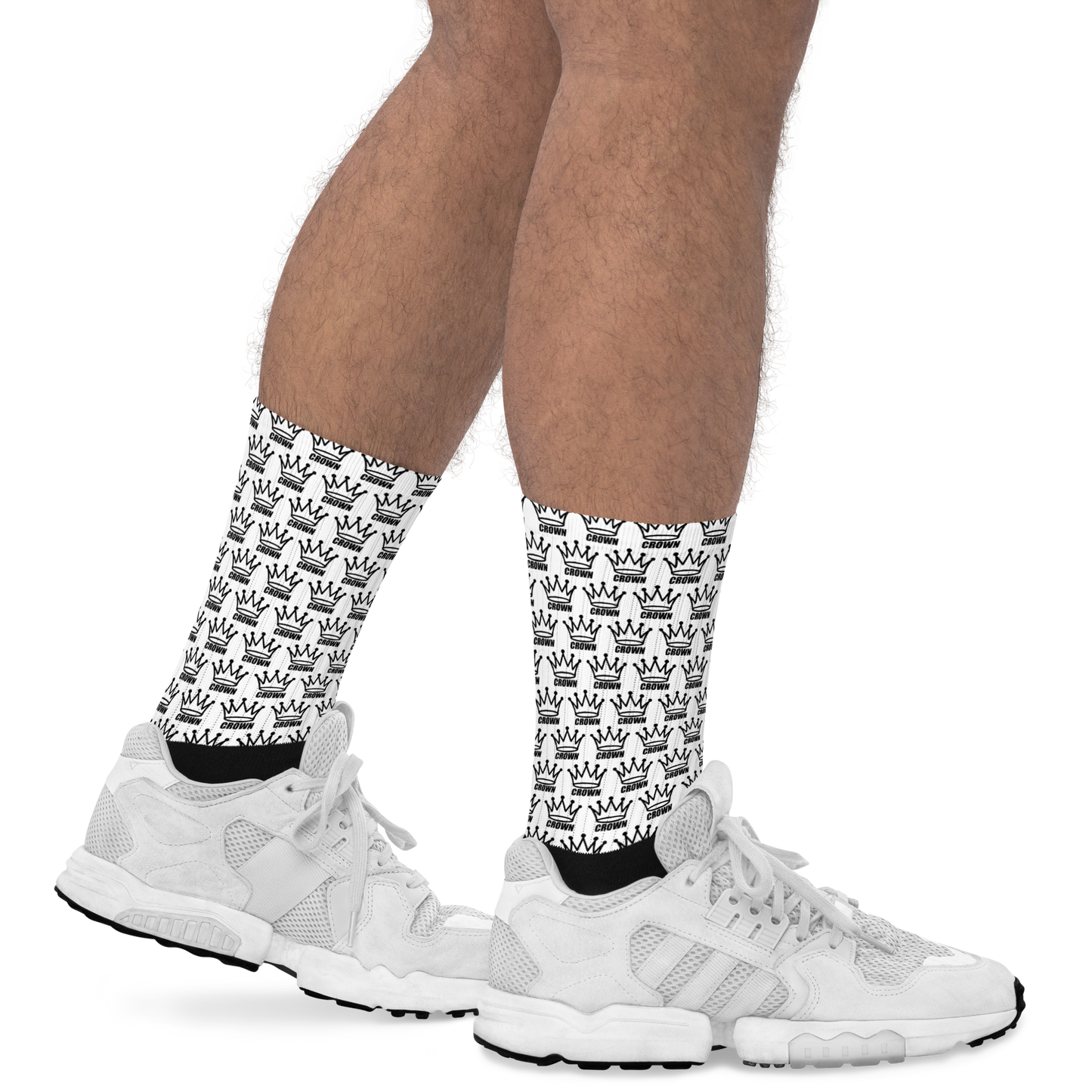 A person wears Crown Pickleball’s CROWN PICKLEBALL - Checkered Crown (White) crew socks, featuring a repeating black crown pattern, with white sneakers. Only their lower legs, socks, and shoes are visible on a white background.